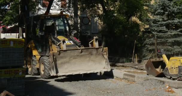 Conductor hombre en ropa de trabajo Excavadora amarilla CAT está conduciendo hacia atrás paletas con bloques Reparación de carreteras pavimentación de la calle de la ciudad Día soleado Polonia Opole — Vídeo de stock