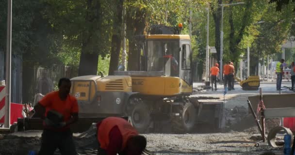 Muži dělníků v žluté oděvy v The Sity Street jsou kopání žlutý bagr Road opravy budovy domy zelené stromy na pozadí dopravní značka — Stock video