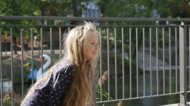 Uzun Adil Saçlar ile Little Girl Ball Catchs Ball Girl Arka Plan Güneşli Günü Park River Boats Ağaçlar Çit Atlama Gülümsüyor Oynuyor