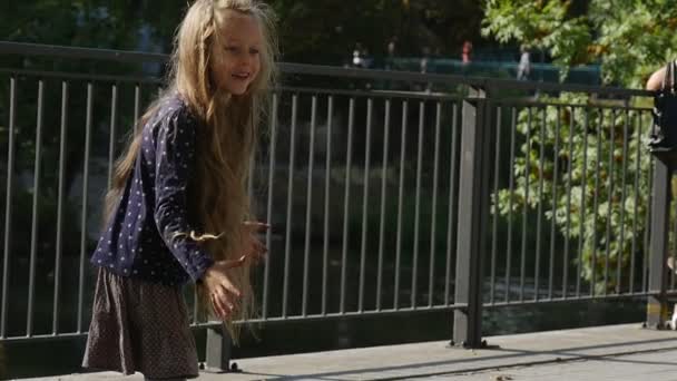 Kleines Mädchen mit langen blonden Haaren spielt Ball fängt das Ballmädchen lächelt springen Park River Boote Bäume Zaun auf Hintergrund sonnigen Tag — Stockvideo