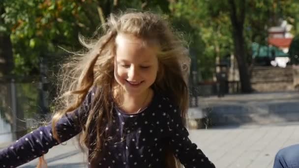 "Lille jente med langt, vakkert hår" "Løper svingende rundt i bakgrunnen" "jente smiler hoppende trær på bakgrundssolskinnsdag". – stockvideo