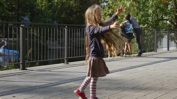 Liten flicka med långa rättvisa hårstrån spelar bollen kastar bollen fångar bollen flickan leende Park människor promenad träd staket på bakgrund solig dag — Stockvideo