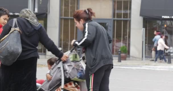 Δύο γυναίκες με καροτσάκι και παρτούζα αγόρι με σακίδια αυτοκινήτου πάνε με πλακόστρωτους δρόμους στην άλλη πλευρά του δρόμου ηλιόλουστη μέρα του φθινοπώρου — Αρχείο Βίντεο
