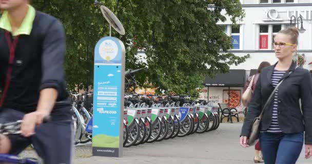 Facet ze słuchawkami jeździ na rowerze ludzie chodzić na chodniku w obu kierunkach parking rowerowy Advertisin Sign Cars go by utwardzona droga słoneczny jesienny dzień — Wideo stockowe