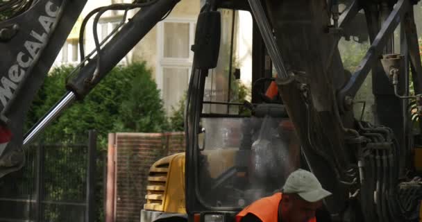 オレンジの労働者が道路を補修道路の舗装をブロックで舗装黄色の掘削機を移動屋根のドライバ上のフラッシャーで閉じるスクープを移動 — ストック動画