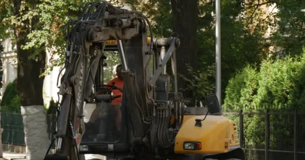 Travailleur en orange vêtements de travail sont sortis de jaune excavatrice route de réparation pavage de la route avec des blocs Ville rue marchant femme arbres verts — Video