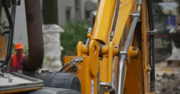 Travailleurs en orange Vêtements de travail à la réparation de la route Excavatrice jaune Gros plan Scoop attrape la poussière de granit paver la route avec des blocs Arbres fond flou — Video