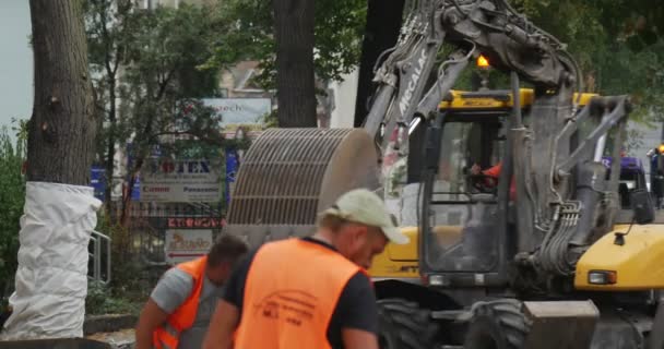 Pracovníci v Orange Workwear Road opravy žluté bagry s blikačkou je pohybující se nákladní automobil stojí dláždění cesty s bloky stromů válcované s Polietilen — Stock video