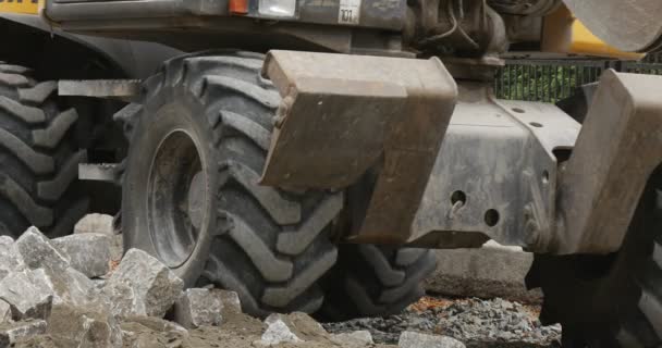 Gelber Bagger Nahaufnahme Roller Haufen von Blöcken Bagger Blätter Räder Nahaufnahme Straßenreparatur Pflaster der Straße mit Blöcken Bäume gerollt mit polietilen — Stockvideo