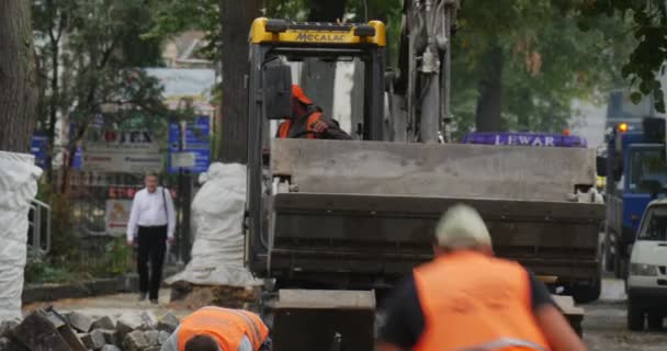 Arbeiders in gele werkkleding op de straat Road Repair Yellow Excavator met Flasher is het verplaatsen van de Scoop terug te draaien Blauwe vrachtwagen bestrating van de weg — Stockvideo