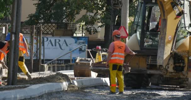 Werknemers in gele werkkleding gele graafmachine kat stuurprogramma is het bewegen van de lading door Scoop bomen op weg reparatie bestrating Road op de straat zonnige dag Polen Opole — Stockvideo