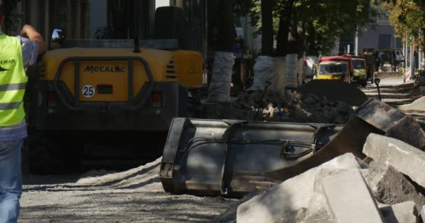 Les travailleurs de Yellow Wokwear marchent dans des sacs pour hommes L'homme pointe vers la pelle jaune sur la route Voitures routières non réparées dans les arbres de rue roulées avec Polietilen — Video