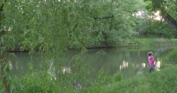 Vista a distancia Niña en la orilla del lago va a pescar acercarse a la cámara — Vídeos de Stock