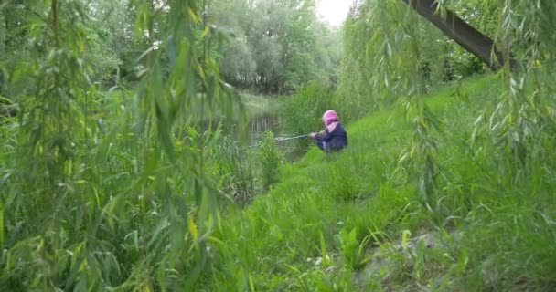 Afstand weergave kind meisje op de oever van het meer gaat vissen — Stockvideo