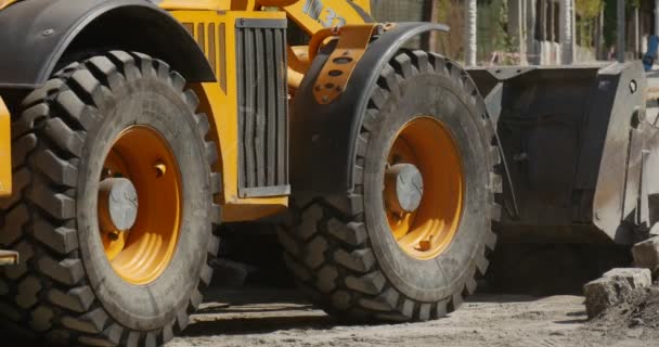 Yellow Excavator Unloads The Heap of Blocks Excavator Wheels Close Up Red Car and Blue Car are Passing by Drivers of Cars Sunny Outdoors Road Repair — Wideo stockowe