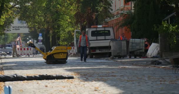 Stojący żółty ręczna maszyna ludzie robotnik w ruchu w kierunku naprawy dróg Nienaprawionych Road Road Sign samochody są przekazując Street Green Trees budynki — Wideo stockowe