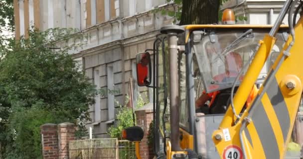 Fahrer steigt in die gelbe Baggerkabine und beginnt Bagger aus nächster Nähe zu bewegen Arbeiter in Arbeitskleidung an der Straße Straßenreparatur Pflaster der Straße — Stockvideo