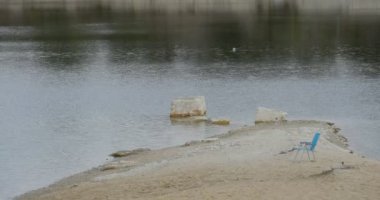 Mavi sandalye Sandy banka Yarımadası dalgalanan su açık havada bulutlu yeşil ağaçlar duruyor