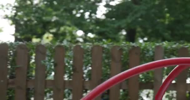 Petite fille aux longs poils blonds en T-shirt orange fait pivoter le carrousel jouant sur le terrain de jeu balançant sur le carrousel avec un jouet rose Tilda Rabbit — Video