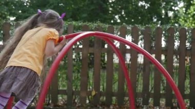 Kız Atlıkarınca Yavaş Hareket Turuncu T-Shirt Uzun Adil Saçlar ile Küçük Kız Swinging Playground Ahşap Çit Yeşil Ağaçlar oynuyor