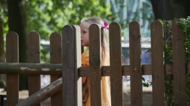 Kız Turuncu T-Shirt Uzun Adil Saçlar ile Ahşap Çit Küçük Kız Kapı ile Bahçeye Girdik Oyun Güneşli Açık Oynuyor