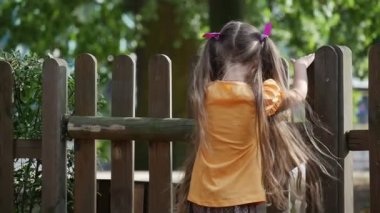 Kız Turuncu T-Shirt Uzun Adil Hairs ile Ahşap Çit Kız Sırt Yavaş Hareket Little Girl Tırmanıyor Oyun Alanı Açık Oynuyor