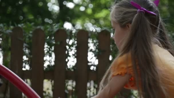 Girl's hoofd nape close-up meisje op carrousel roterende carrousel meisje met lange eerlijke haren in oranje T-shirt speelt buiten in de speeltuin — Stockvideo