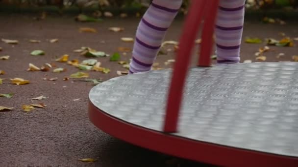 Mädchen dreht das Karussell rosa Spielzeugkaninchen auf Karussell kippt kleines Mädchen mit langen blonden Haaren in orangefarbenem T-Shirt spielt s auf dem Spielplatz — Stockvideo