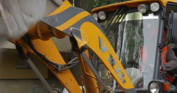 Werknemers in oranje werkkleding Road repareren gele graafmachine dicht omhoog Scoop lost het graniet stof stuurprogramma in cabine effenen de weg met blokken — Stockvideo