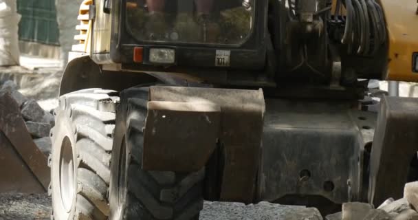 Grävmaskin närmar sig blocken med Scoop närbild förare arbetare i orange Workwear väg reparation stenläggning av vägen med block City Street — Stockvideo