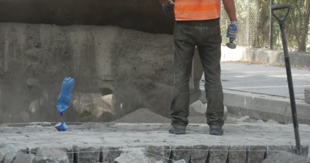 Trabajador en Orange Workwear Excavadora amarilla descarga la cuchara de polvo de granito de cerca en los bloques que pavimentan el camino con bloques Roar Repair Poland Opole — Vídeo de stock