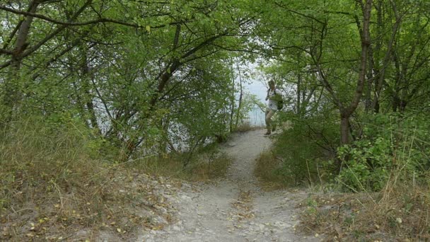 Man toerist man met rugzak man komt van achter de struiken lopen door voetpad onder de groene heuvel top naar beneden weergave groene Buches groene bomen — Stockvideo