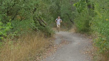 Sırt Çantası ile Beyaz T-Shirt Man Turist Man Kamera Overgrown Hill Yavaş Hareket Yeşil Ağaçlar Green Hill Yaklaşımlar Footpath tarafından Çalışıyor