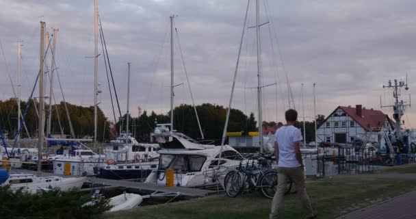 Man går till piren vita båtar läggs upp Yacht Club Port hamnen lugn klart vatten molnig himmel solnedgång sommaren Leba Polen — Stockvideo