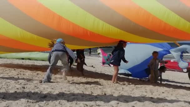 Gyerekek nyomja egy színes Conic levegőben úszó a levegőben, kipróbálás-hoz csinál ez fogás a szél alatt a nemzetközi kite Fesztivál, Łeba, Lengyelország. — Stock videók
