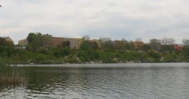 Bir Ufukta Ön Planda Saz bulutlu Gökyüzü Evleri üzerinde River Lake Dalgalanan Su Green Hill Footpathes üzerinde Kırmızı Evler Binalar