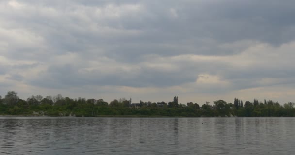Річка озеро ставок брижами води крупним планом плаваючі хмари зелені дерева на горизонті в протилежному березі хмарний небо на відкритому повітрі денний пейзаж — стокове відео