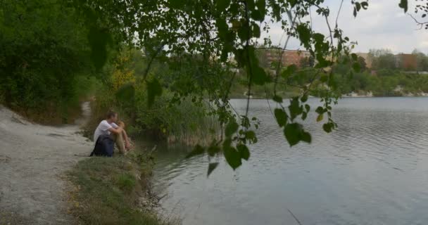Homme touriste homme en blanc T-shirt homme avec sac à dos est assis au sac à dos de l'eau Bâtiments Les maisons sont à la rive opposée sur un horizon Journée en plein air — Video