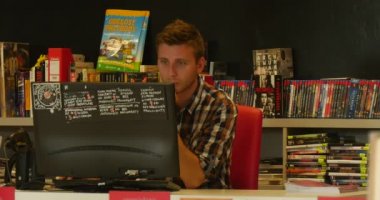 Ekose gömlekli adam bilgisayar kütüphaneci raflardan kitap ve diskler John Paul II Belediye Halk Kütüphanesi Opole Polonya'da arka plan satırları üzerinde çalışıyor