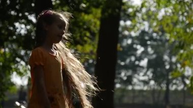 Kız dönüm güneş gülümseyen ağır çekim küçük kız ile uzun adil tüyleri iki Ponytails leylak yay turuncu tişört kıza Bahçesi adlı civarındadır