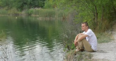 Adam turist adam beyaz T-Shirt adam su adam yeşil ağaçlar açık havada bulutlu gündüz arasında dalgalanan nehir kıyısında, sırt çantası ile