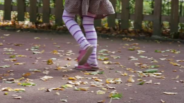 Девочка ноги крупным планом идет к карусели держа розовый игрушечный кролик маленькая девочка с длинными светлыми волосами в оранжевой футболке играет на детской площадке — стоковое видео