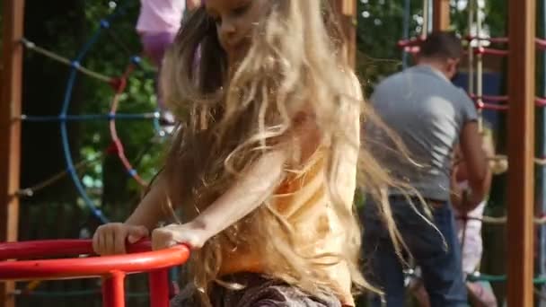 Flickan svänger på en gunga med sin leksak kanin rosa Tilda svänga på en swing liten flicka med långa rättvisa hårstrån i orange T-shirt på lekplatsen — Stockvideo