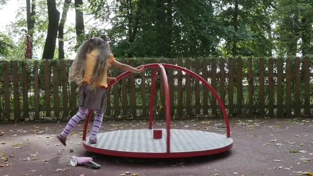 소녀는 회전 목마 핑크 장난감 틸다 토끼에 스윙오렌지 티셔츠에 긴 공정한 머리카락을 가진 어린 소녀가 놀이터에서 야외에서 놀고있다 — 비디오
