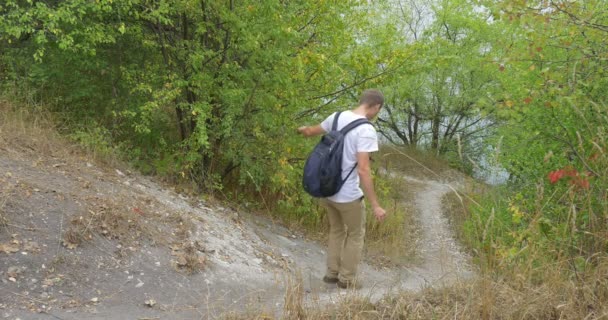 Man τουρίστας άνθρωπος με λευκό μπλουζάκι με σακίδιο είναι περπατώντας προς τα κάτω τρέξιμο με μονοπάτι στο δάσος Green Hill πάρκο πράσινα δέντρα νωρίς το φθινόπωρο — Αρχείο Βίντεο