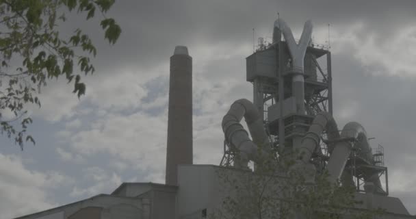 Zilveren buizen van de fabriek wolken rook tak met groene bladeren ecologie vervuiling van milieu stof cement fabriek Opole Polen — Stockvideo