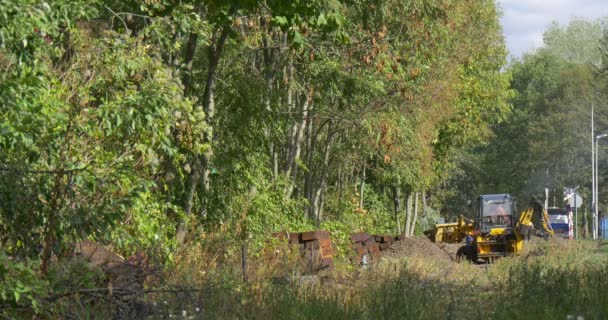 Дистанционно работающие землекопы копают жёлтый экскаватор выгружает земляное здание на лесной дороге Гроув на заднем плане Автомобили на дороге — стоковое видео