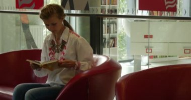 Kadın kırmızı kanepede oturur ve okur kitap sonra o kitap ayağa kalkar ve Dış Saha John Paul II Belediye Halk Kütüphanesi Opole Polonya gider kapanır