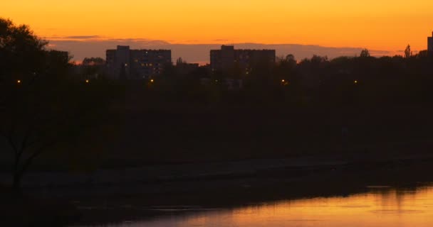 Řeka bank u přehrady na řece River v městě jasná žlutá obloha odraz odrazu s hladkými vodními domy jasně žlutá siluety stromů slunce — Stock video