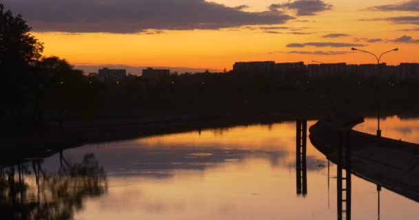 Barrage sur le barrage de la rivière à la digue de la ville prend en charge le reflet de l'eau lisse Maisons résidentielles Silhouettes des arbres de coucher de soleil jaune vif — Video